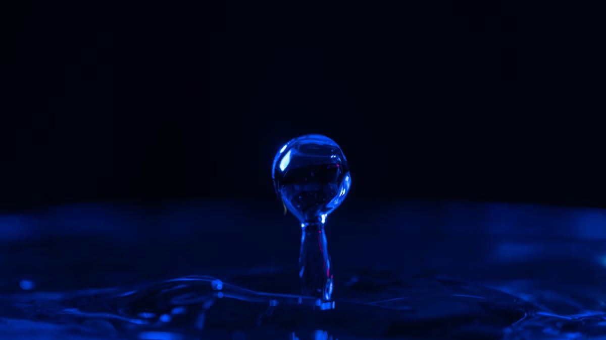 Macro image capturing a single, blue-illuminated water droplet in motion, creating a dramatic effect.